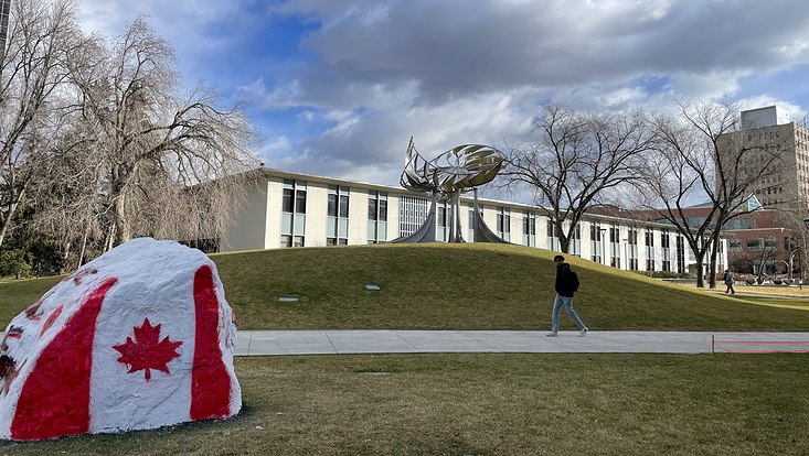 Bild vom Campus der University of Calgary. Im Vordergrund ein großer Stein, auf den die Kanadische Flagge gemalt ist