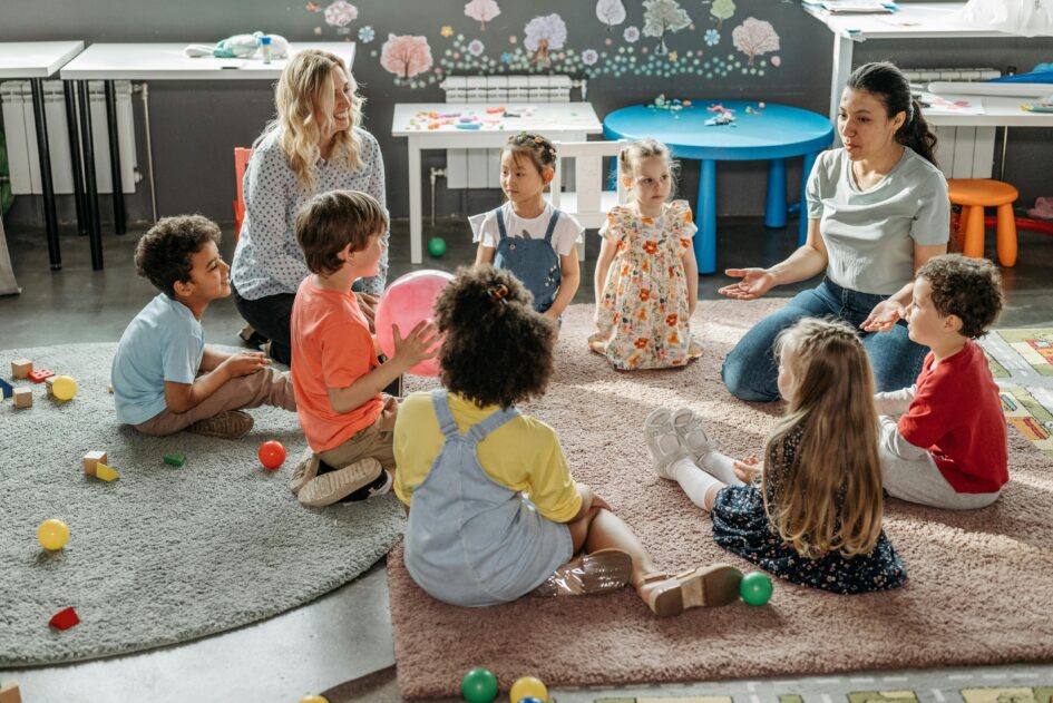 Kinder sitzen in einem Kreis und reden mit zwei Kindergärtnerinnen.